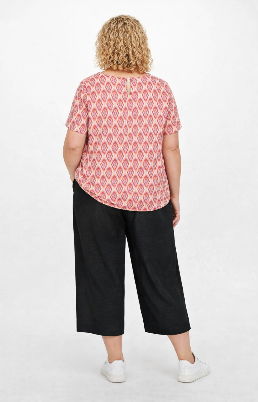 Woman wearing a pink patterned top and black pants on a white background
