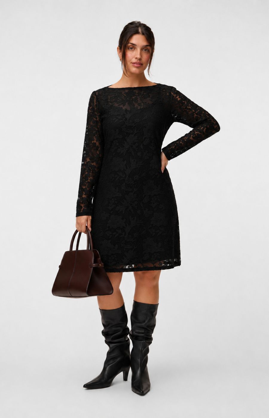Model wearing the Vero Moda Curve Layla Dress in Black, a knee length black lace dress with a boat neckline and long sleeves. This image was created using AI