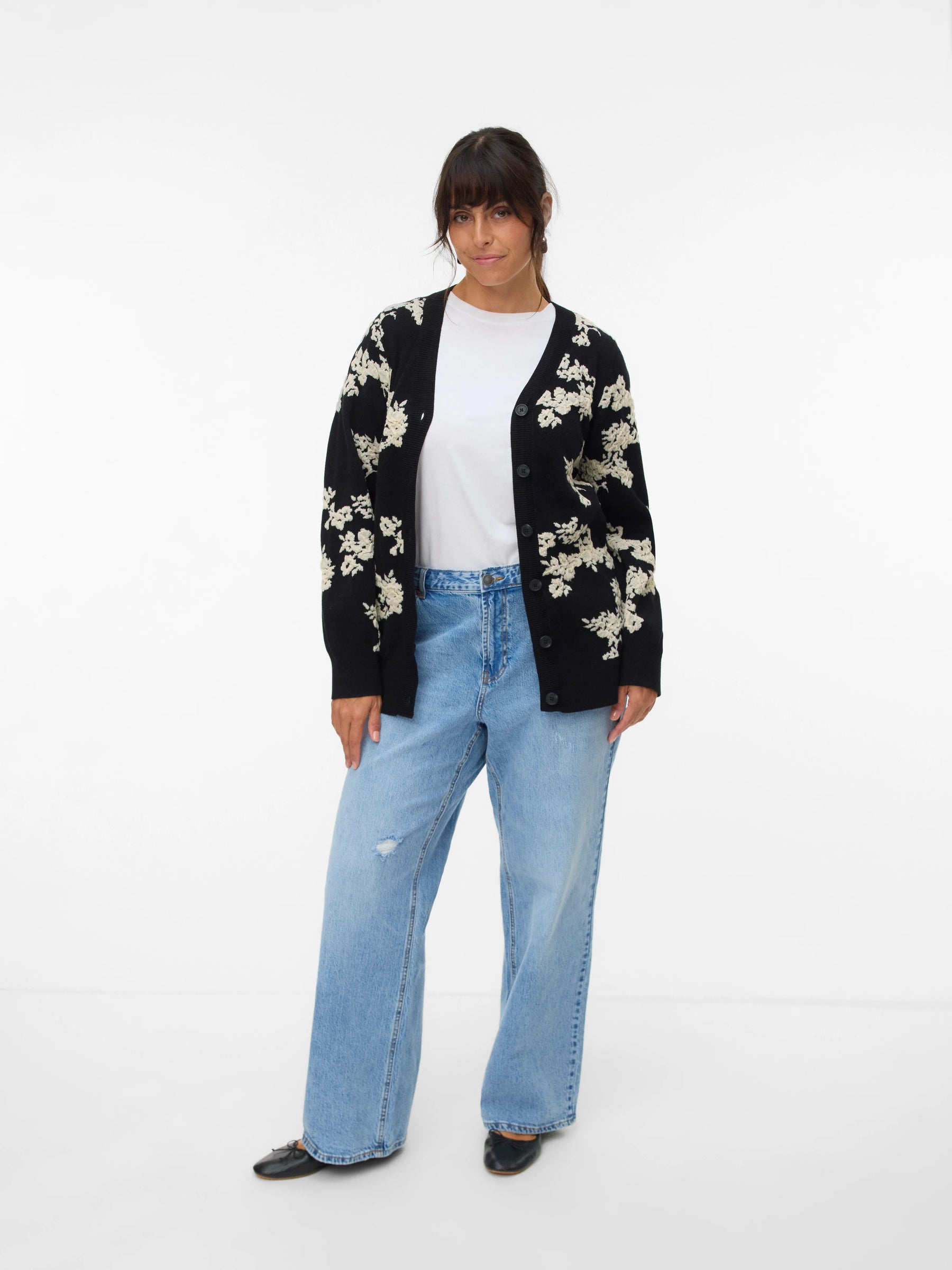 Person wearing a black floral cardigan, white shirt, and light blue jeans on a white background