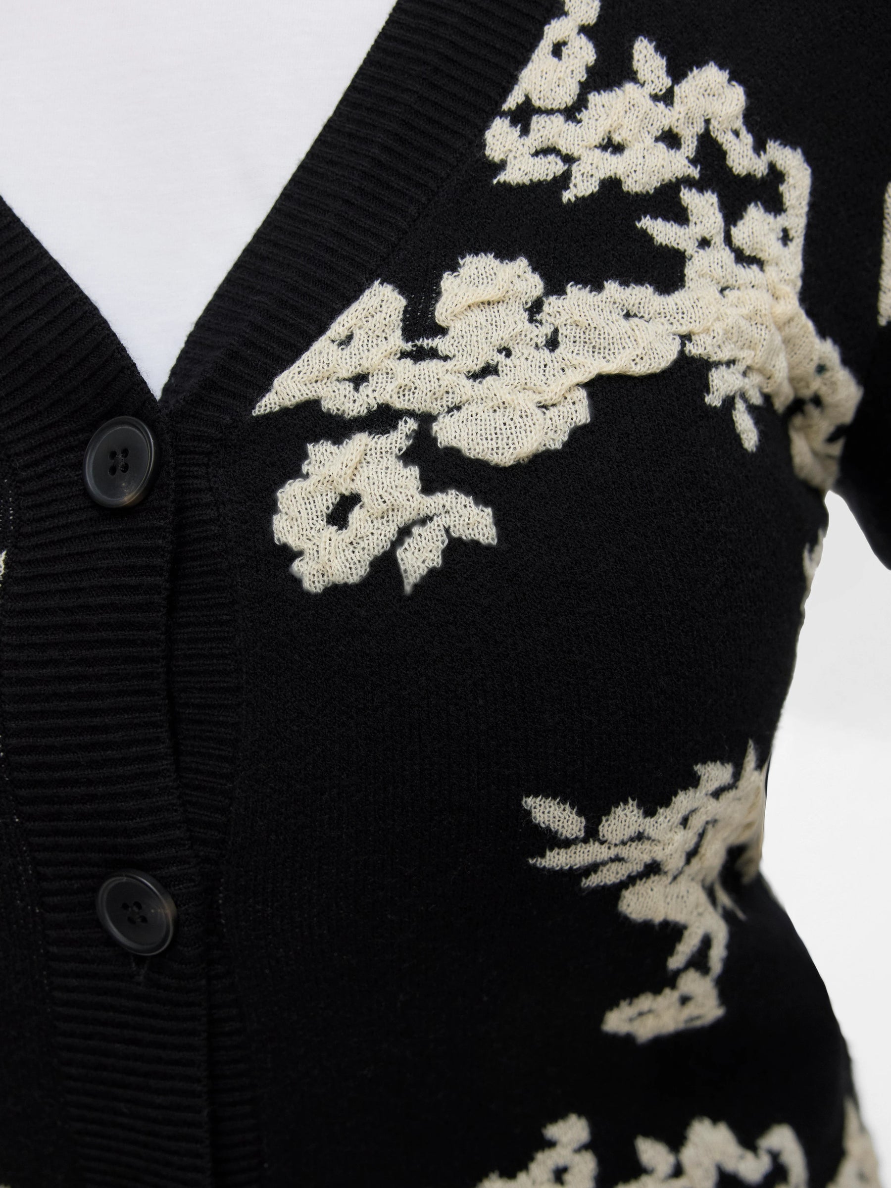 Black cardigan with white floral embroidery on a plain background