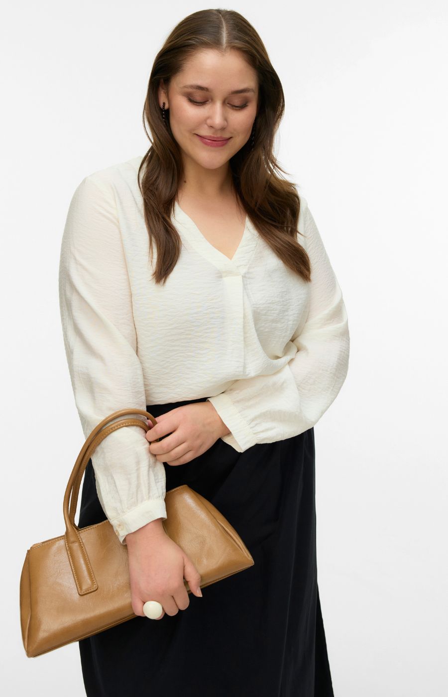 Woman wearing a white blouse with a V neckline and long sleeves, and black skirt holding a brown handbag on a white background