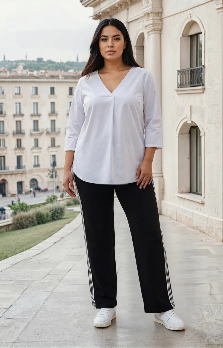 Woman wearing a white blouse and black pants standing in front of a building.