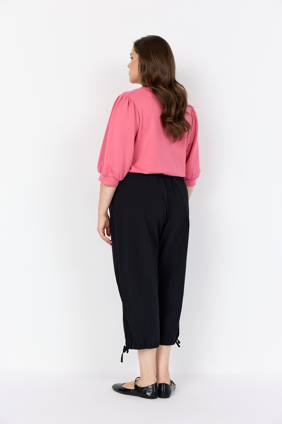 Woman wearing a Wasabi Sabina Blouse in Pink with 1/2 length sleeves and black pants against a white background