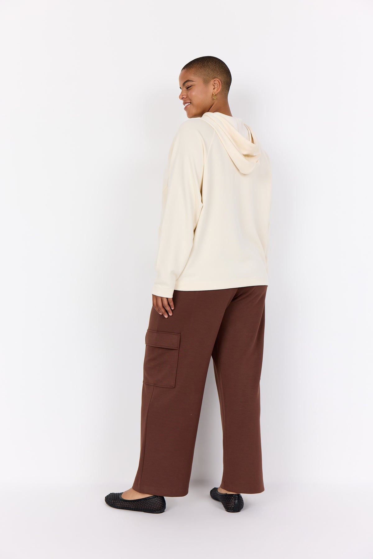 Person wearing a Wasabi Sabina Hoodie in Cream, a long sleeves hoodie and brown pants against a white background