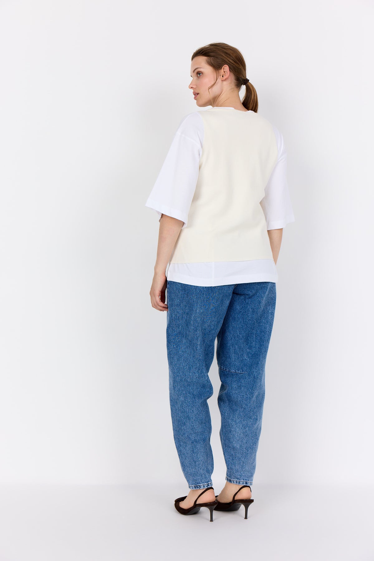 Woman wearing a Wasabi Sikka Waistcoat in Cream, and blue jeans against a white background