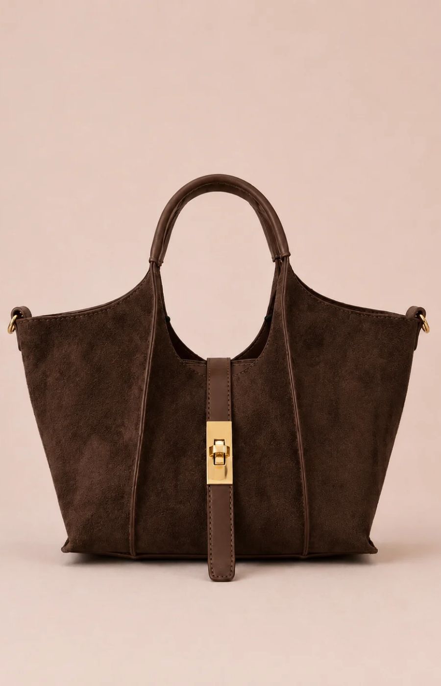 A dark brown suede tote bag with a central gold-tone turn-lock clasp and a matching hanging strap, set against a solid pale pink background.