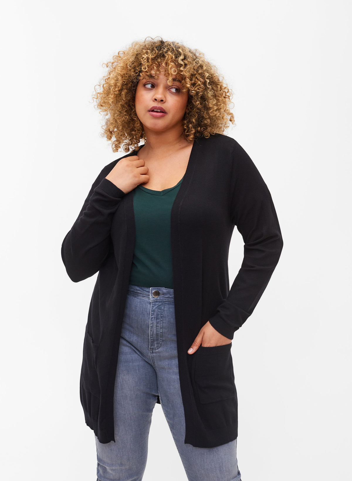Woman wearing a black long line cardigan over a green top and blue jeans on a white background