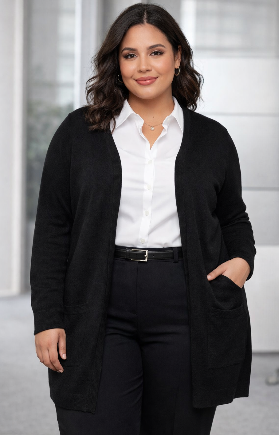 Woman wearing a black cardigan over a white shirt and black trousers in an indoor setting.