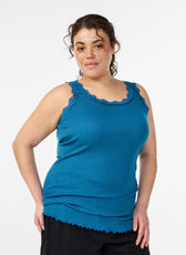 Woman wearing a teal tank top with lace trim on a white background