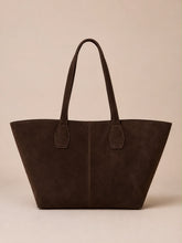 A dark brown suede tote bag with long shoulder straps, photographed against a solid beige background.