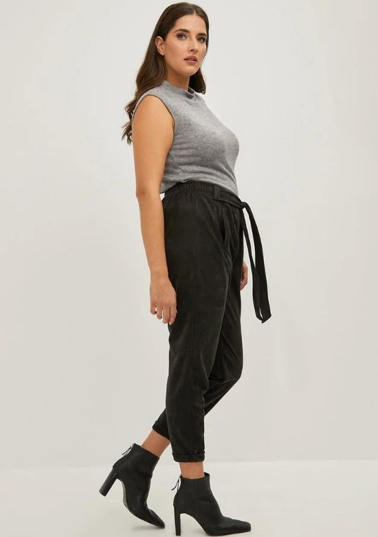A woman standing up. She is wearing black Mat faux suede harem trousers and a silver sleeveless top.