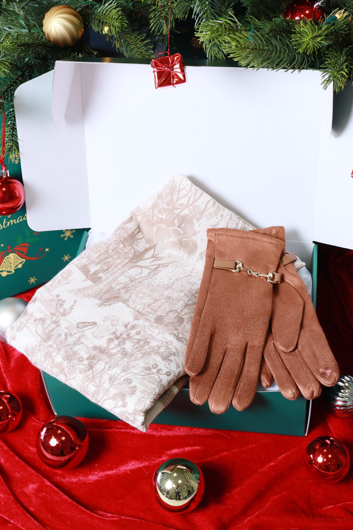 Brown gloves with a gold charm on a white surface next to a red fabric and Christmas decorations.