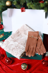 Brown gloves with a gold charm on a white surface next to a red fabric and Christmas decorations.