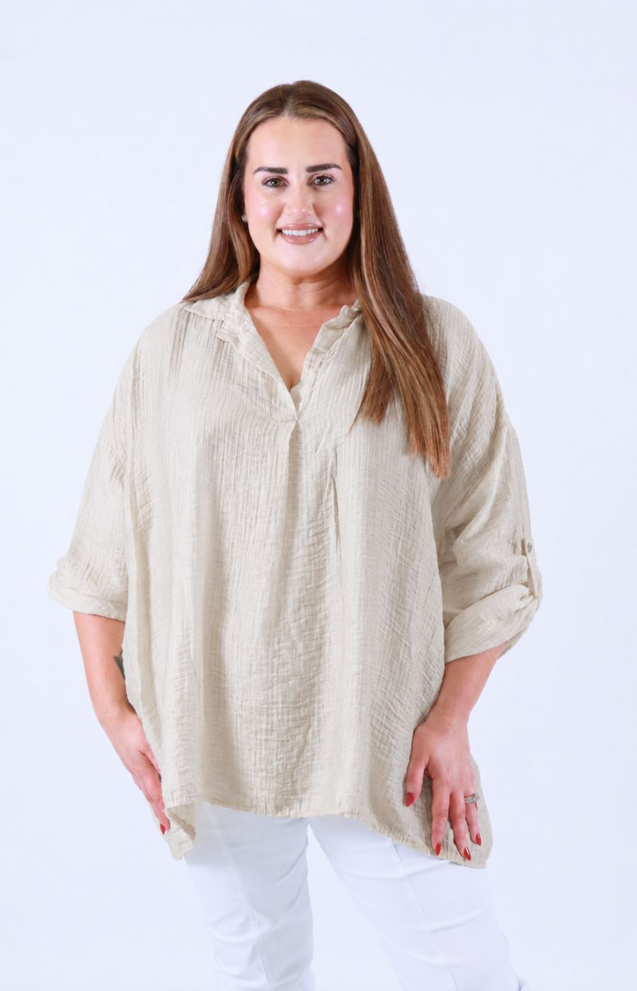 Woman wearing the Ellie V Neck Blouse in Beige, a beige textured shirt and white pants on a white background