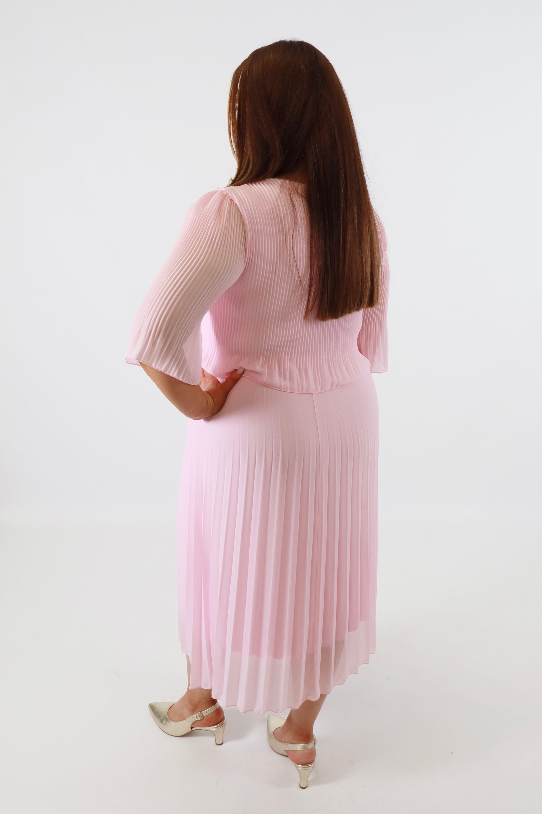 Plus size woman wearing a pink pleated dress with gold shoes on a white background