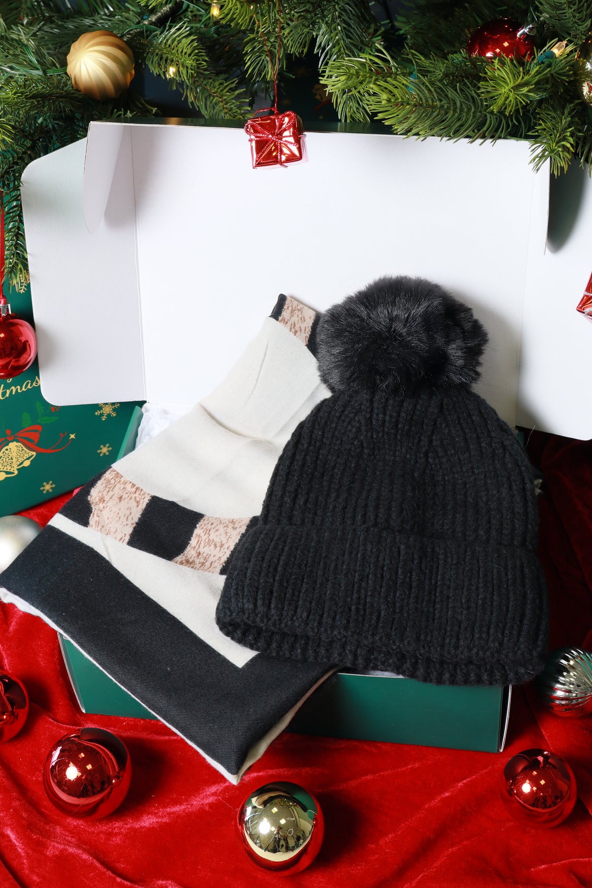 Black knit hat with pom-pom on a white surface surrounded by Christmas decorations.