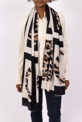 Person wearing a long, patterned scarf with geometric and animal print designs on a white background.