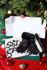 Black gloves with white pattern on a white box, surrounded by Christmas decorations.
