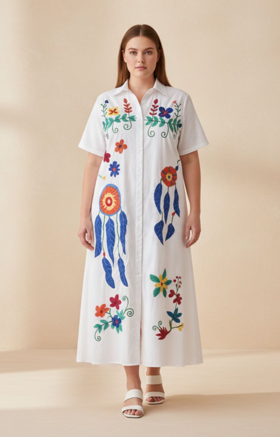 Woman wearing the Fern Floral Dress in White, a white dress with colorful floral and abstract designs on a beige background