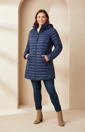 Plus size woman wearing a navy coat, dark blue jeans and brown boots on a cream background