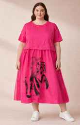 Woman wearing the bright pink Gemma dress with black abstract design, mesh netting to the side, soft, stretchy cotton top, on a beige background