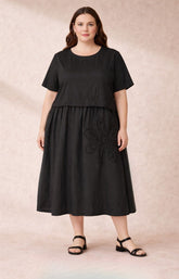 Geneva Dress in Black, a cotton dress with an A-line shape, round neckline, short sleeves, side pockets and a floral applique design on the front