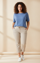 Woman wearing a blue top and beige pants against a beige background