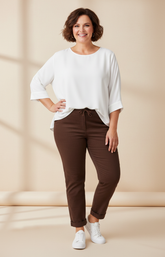 Woman wearing a white top and brown pants on a beige background
