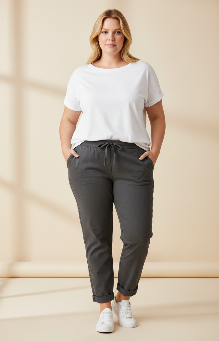 Woman wearing a white t-shirt and dark gray pants against a beige background