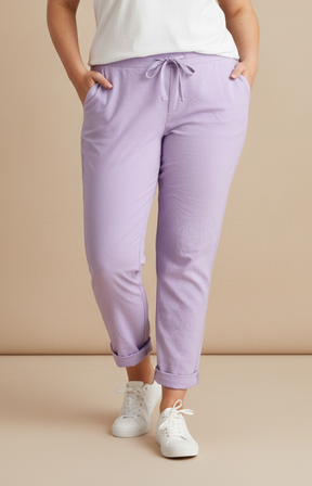 A plus size woman wearing lilac joggers and a white t-shirt on a cream background