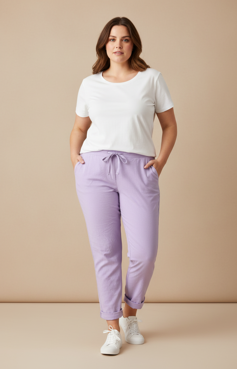 A plus size woman wearing lilac joggers and a white t-shirt on a cream background