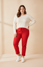 A plus size woman wearing red joggers and a cream long sleeve top on a beige background