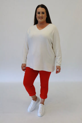 A plus size woman wearing red joggers and a white long sleeve top on a beige background