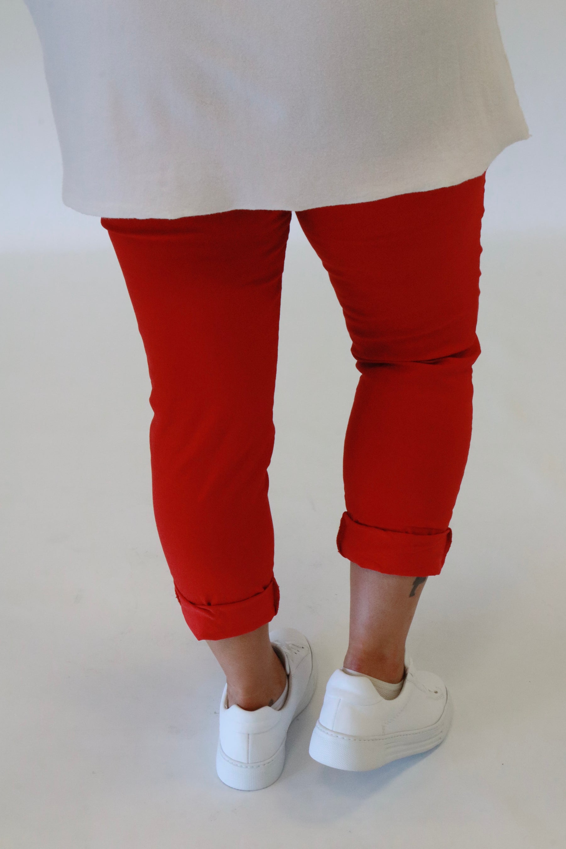 A plus size woman wearing red joggers and a white long sleeve top on a beige background