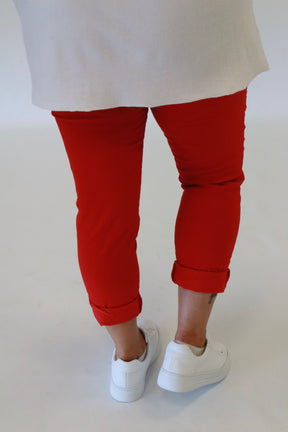 A plus size woman wearing red joggers and a white long sleeve top on a beige background