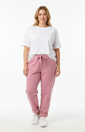 Plus size model wearing a white short-sleeve T-shirt and pink elastic waist trousers with tie belt and rolled cuffs, styled with white runners.