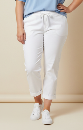 A plus size woman wearing white trousers, blue t-shirt and white trainers on a beige background