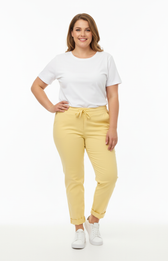 A curvy woman wearing yellow joggers and a white t-shirt on a white background