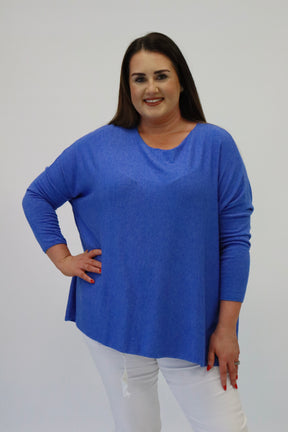 Woman wearing a blue sweater and white pants against a plain background