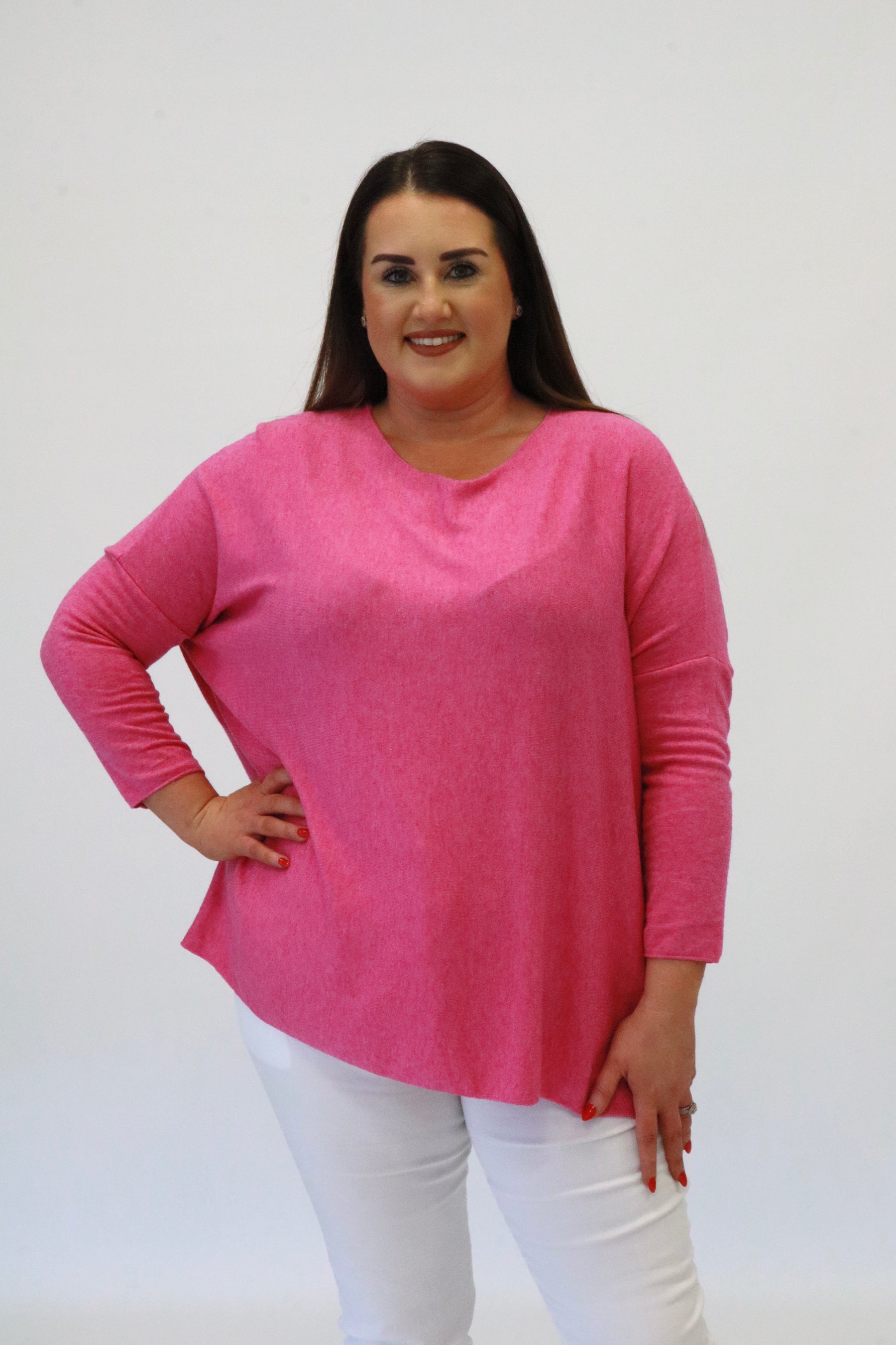 Woman wearing a pink sweater and white pants against a plain background