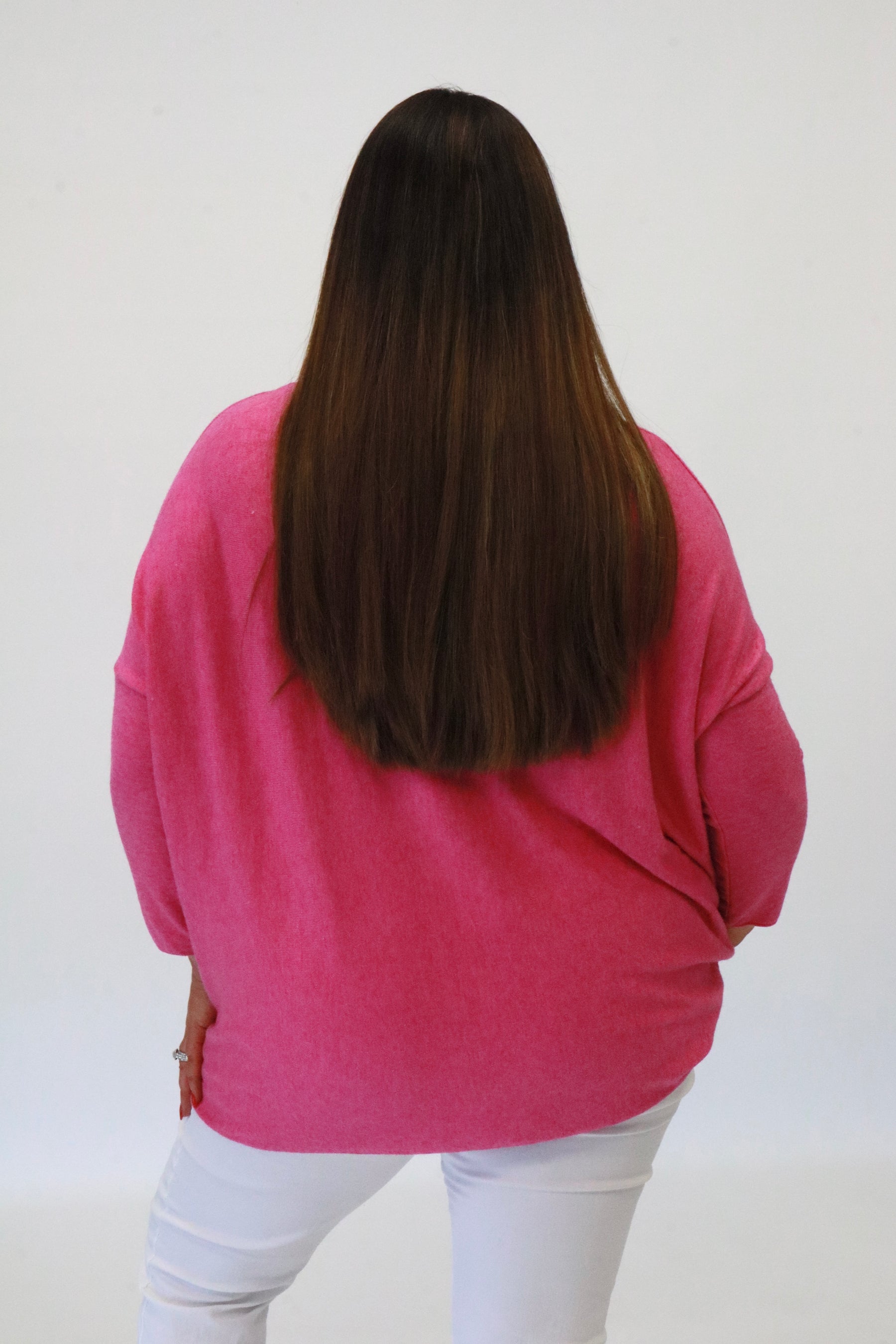 Person wearing a pink sweater and white pants against a plain background