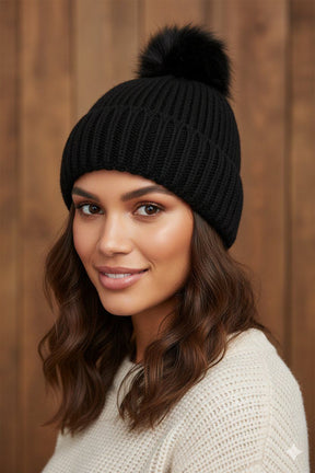 Woman wearing a black knit beanie with a pom-pom against a wooden background