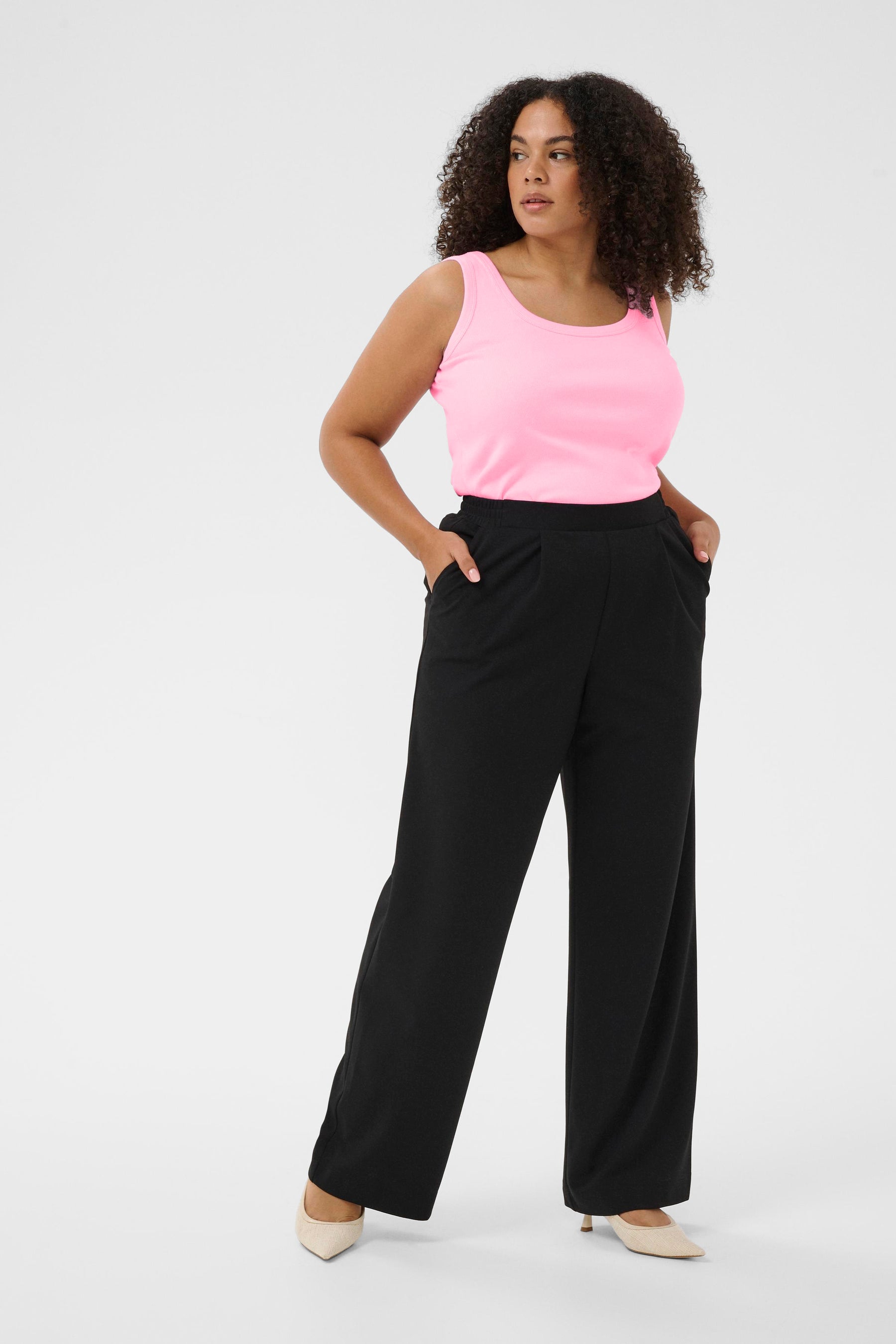Woman wearing a light pink sleeveless top and black wide-leg pants on a white background