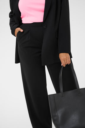 Person wearing a black suit with a pink vest top, holding a black tote bag on a white background