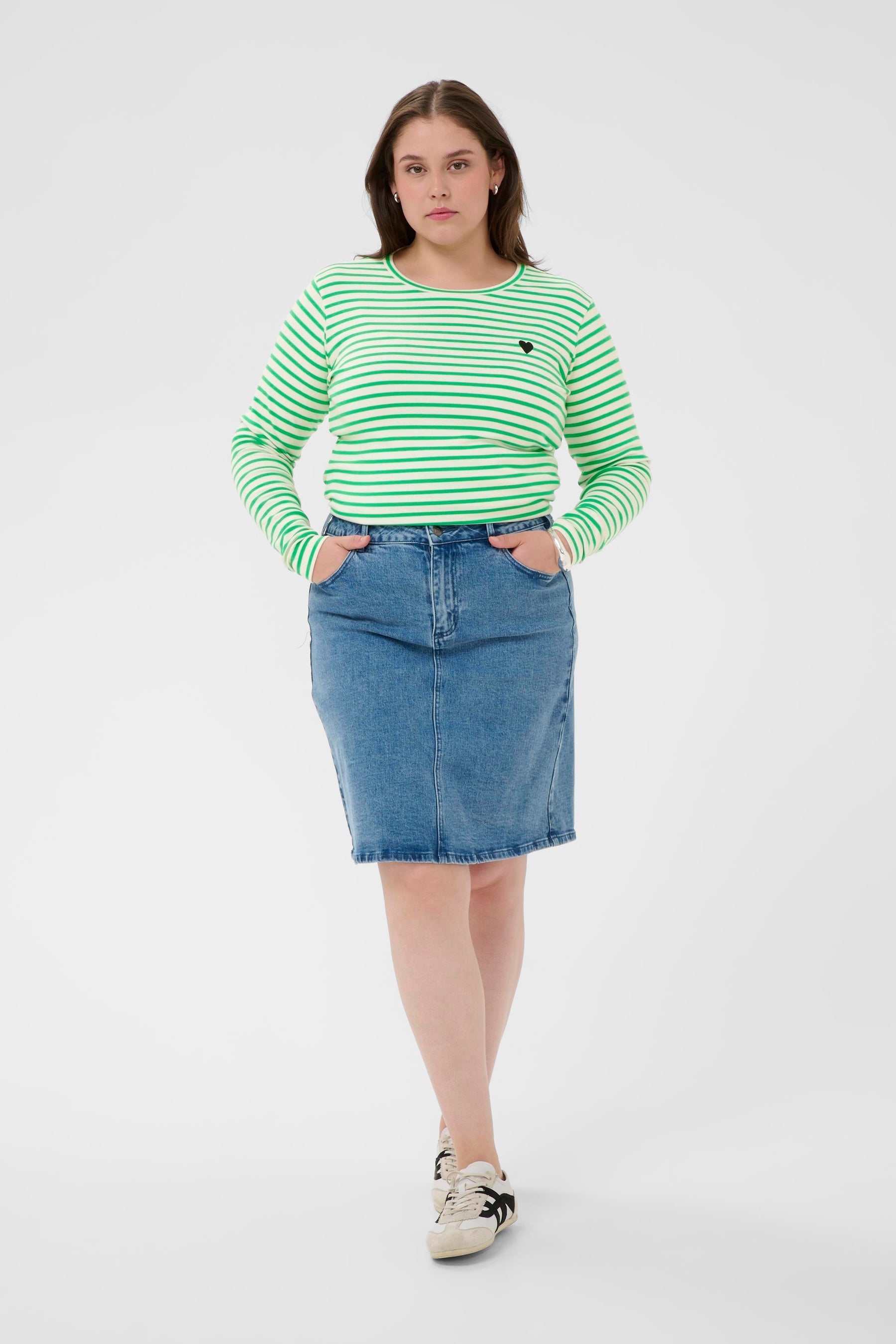 Woman wearing a green and white striped shirt and blue denim skirt on a white background 