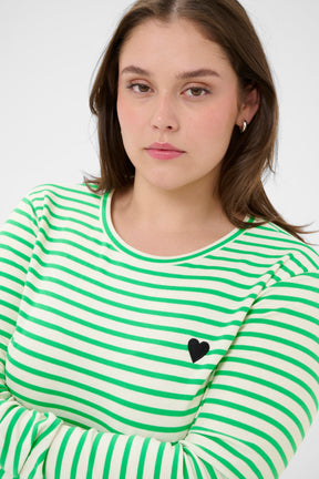 Woman wearing a green and white striped shirt with a black heart on a plain background
