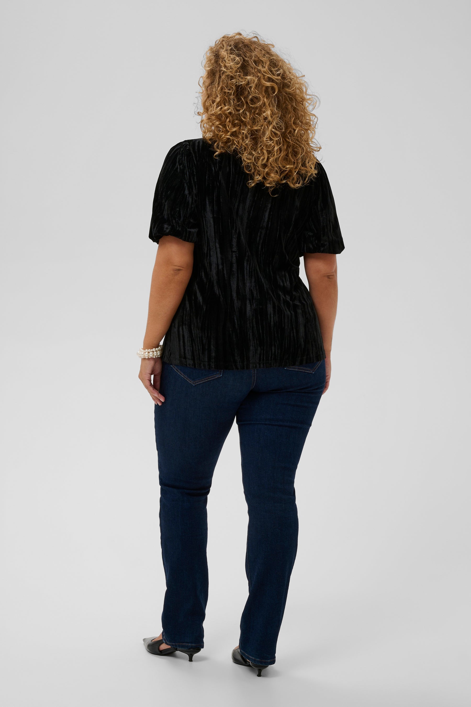Person wearing a black textured top and blue pants on a white background