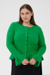 Woman wearing a green cardigan with long sleeves, round neckline, silver buttons, ruffle detailing on the cuffs and hem against a white background