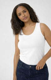 Woman wearing a white tank top with a round neckline and dark blue jeans against a plain background