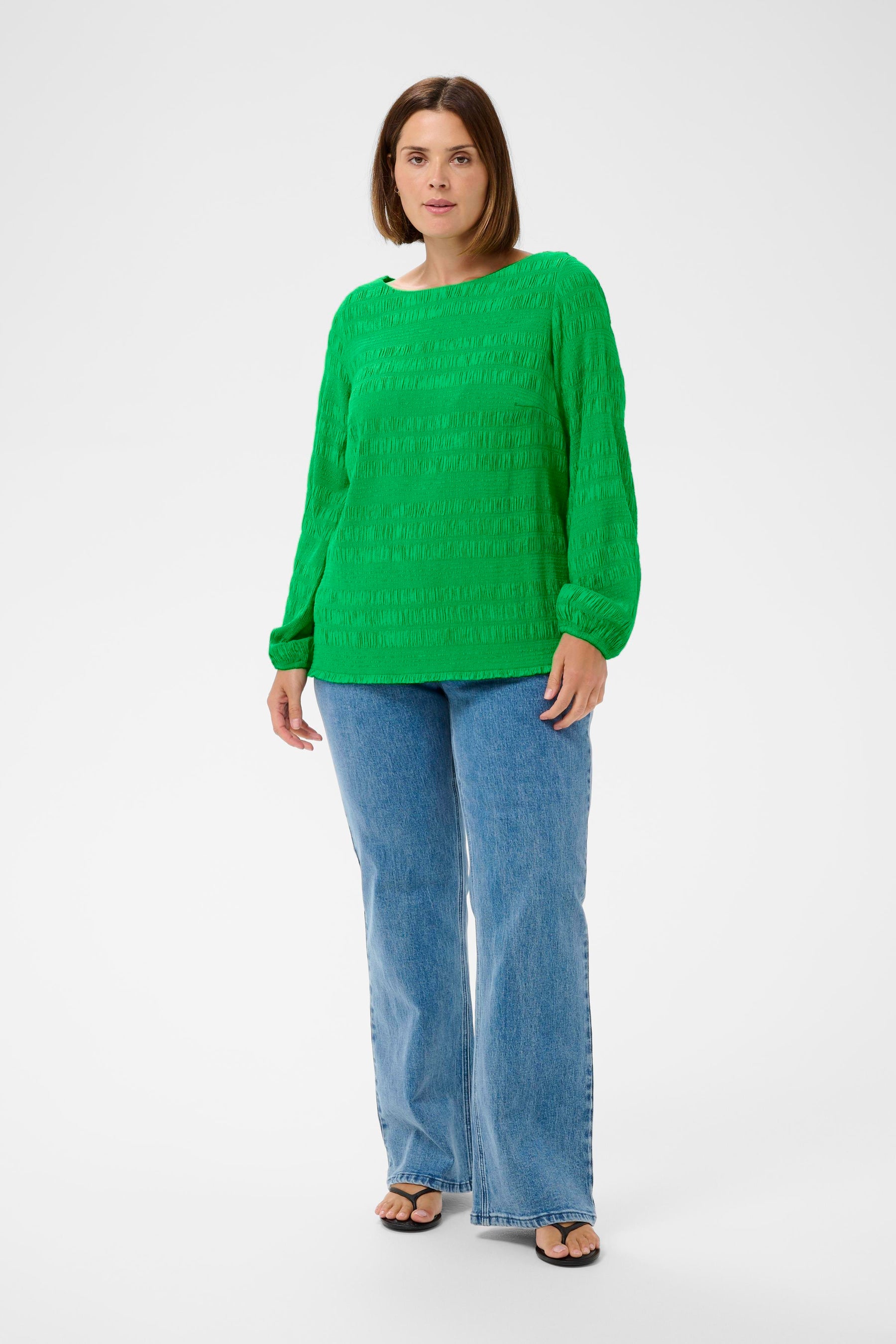 Woman wearing Kaffe Curve Jourtney Blouse in Greenand blue jeans on a white background